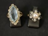 two rings with a blue topaz and a pearl on a black surface