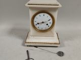 a small white clock with a gold face and a key