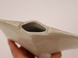 a hand holding a white vase with a small hole in it