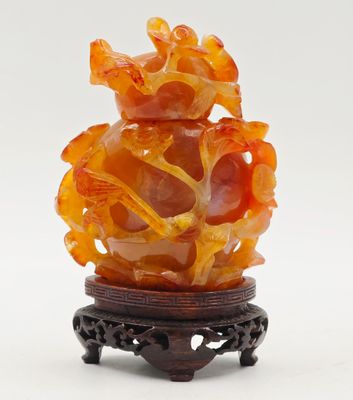 Vase chinois en jade orange sculpté, posé sur un socle, sur fond blanc