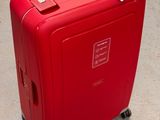 une valise rouge posée par terre, sur laquelle est accrochée une étiquette de prix
