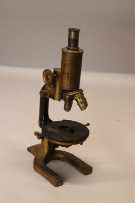 Un vieux microscope est posé sur une table avec un fond blanc.