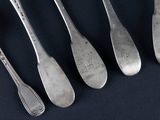 six spoons and a fork are lined up on a black surface