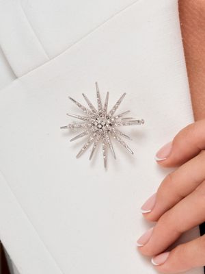 La femme porte une robe blanche et tient une broche argentée.