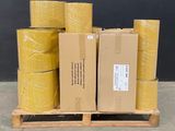 Plusieurs rouleaux de ruban adhésif jaune sont empilés sur une palette devant un mur noir.