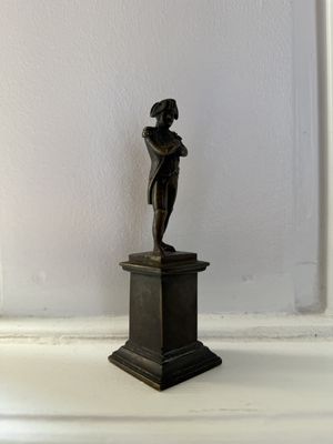 une petite statue en bronze représentant une femme, posée sur un socle