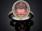 a close up of a ring with a pink stone surrounded by diamonds