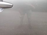 a man standing in the fog with his reflection in a car mirror