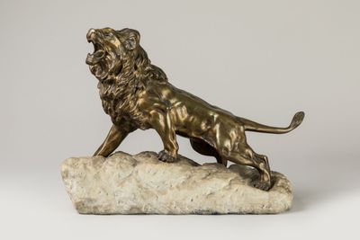 une statue en bronze représentant un lion posé sur un rocher, sur fond blanc