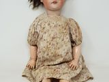 une poupée à l'ancienne, assise sur une surface blanche, vêtue d'une robe et de chaussures