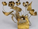 des fleurs en laiton dans un vase posé sur un socle en bois, sur fond blanc