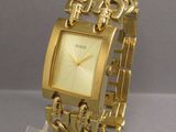 a gold watch on a clear stand on a gray surface