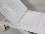 underside view of a white plastic lawn chair with wheels on a white background