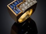 a gold ring with sapphire and diamonds on a black surface