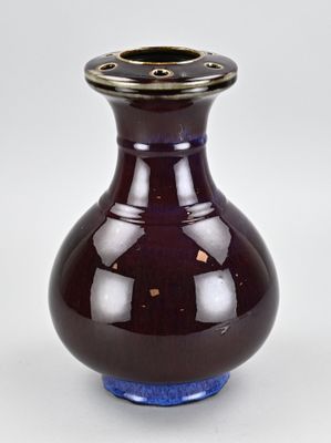 un vase violet bordé d'or posé sur une surface blanche
