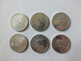 six different coins are shown in a row on a white surface