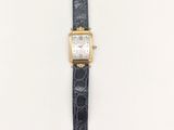 une montre en or avec un bracelet en cuir noir et un cadran blanc
