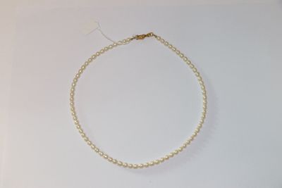 un collier de perles blanches avec une chaîne en or posé sur une surface blanche