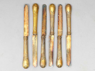 six cuillères en argent et un couteau sont alignés sur une surface blanche