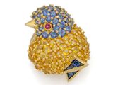 un gros plan d'une broche en forme d'oiseau ornée de pierres bleues et jaunes