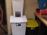 a white trash can sitting next to a trash can in a kitchen