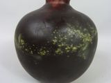 un vase noir parsemé de taches vertes, posé sur une surface blanche