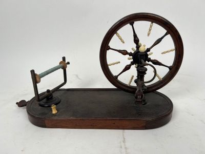 une petite machine à filer avec un socle en bois posée sur une surface blanche