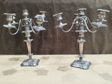 two silver candelabs on a table with a brown background