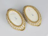 a pair of gold and white oval shaped dishes on a white surface