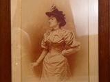 une vieille photo représentant une femme en robe et chapeau, dans un cadre en bois