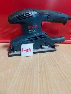 une ponceuse orbitale Bosch posée sur une table, à côté d'une boîte rouge