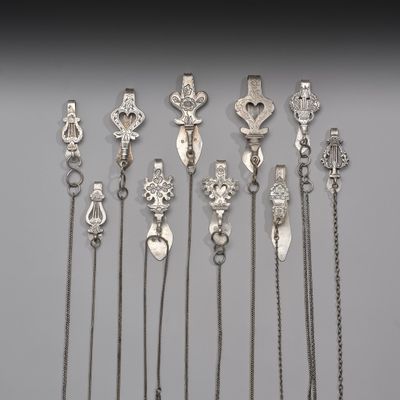 Plusieurs cuillères et chaînes en argent sont disposées sur une surface grise