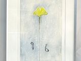 painting of a single yellow flower in a white frame on a table