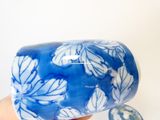 une main tenant un vase bleu et blanc orné de fleurs blanches
