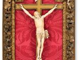 un crucifix en bois accroché à un mur rouge, dans un cadre doré