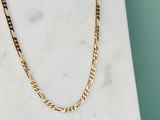 un collier à chaîne en or posé sur une dalle de marbre