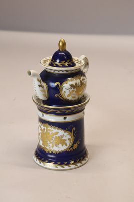 une théière bleue et dorée avec son couvercle, posée sur une table blanche