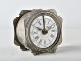 a small silver clock with roman numerals on it