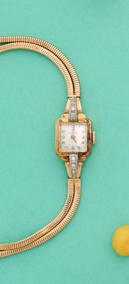 une montre en or et un bracelet en or posés sur une surface verte