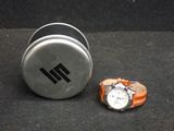 une montre posée à côté d'une canette sur laquelle figure un logo