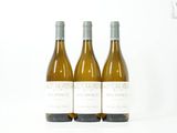 trois bouteilles de vin blanc posées l'une à côté de l'autre sur une surface blanche