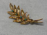 a close up of a gold leaf brooch with green stones