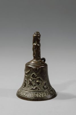 une vieille cloche en bronze posée sur une surface blanche, avec un fond gris