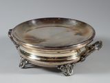 un plat ancien en argent avec des poignées, posé sur un socle, sur fond blanc