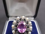 une photo d'une bague en pierre rose et perle dans un écrin bleu
