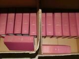 Plusieurs livres roses se trouvent dans une boîte en carton posée sur une table