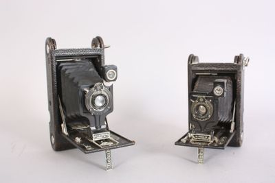 two old cameras sitting side by side on a white surface