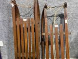 Plusieurs luges en bois sont alignées contre un mur gris