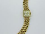 a gold bracelet watch with a white face on a white surface