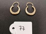 a pair of gold hoop earrings and a tag on a black surface